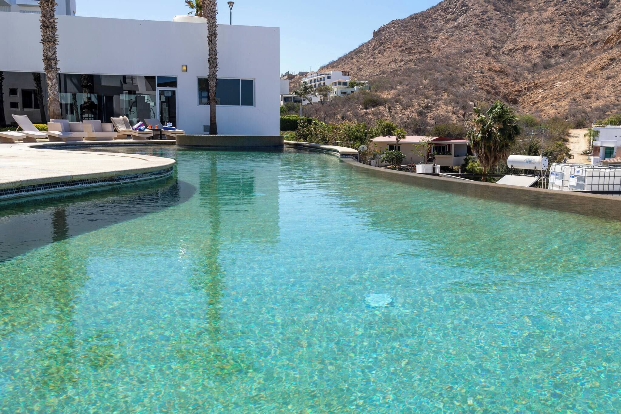 Una piscina limpida con sedie a sdraio e un edificio moderno sullo sfondo.