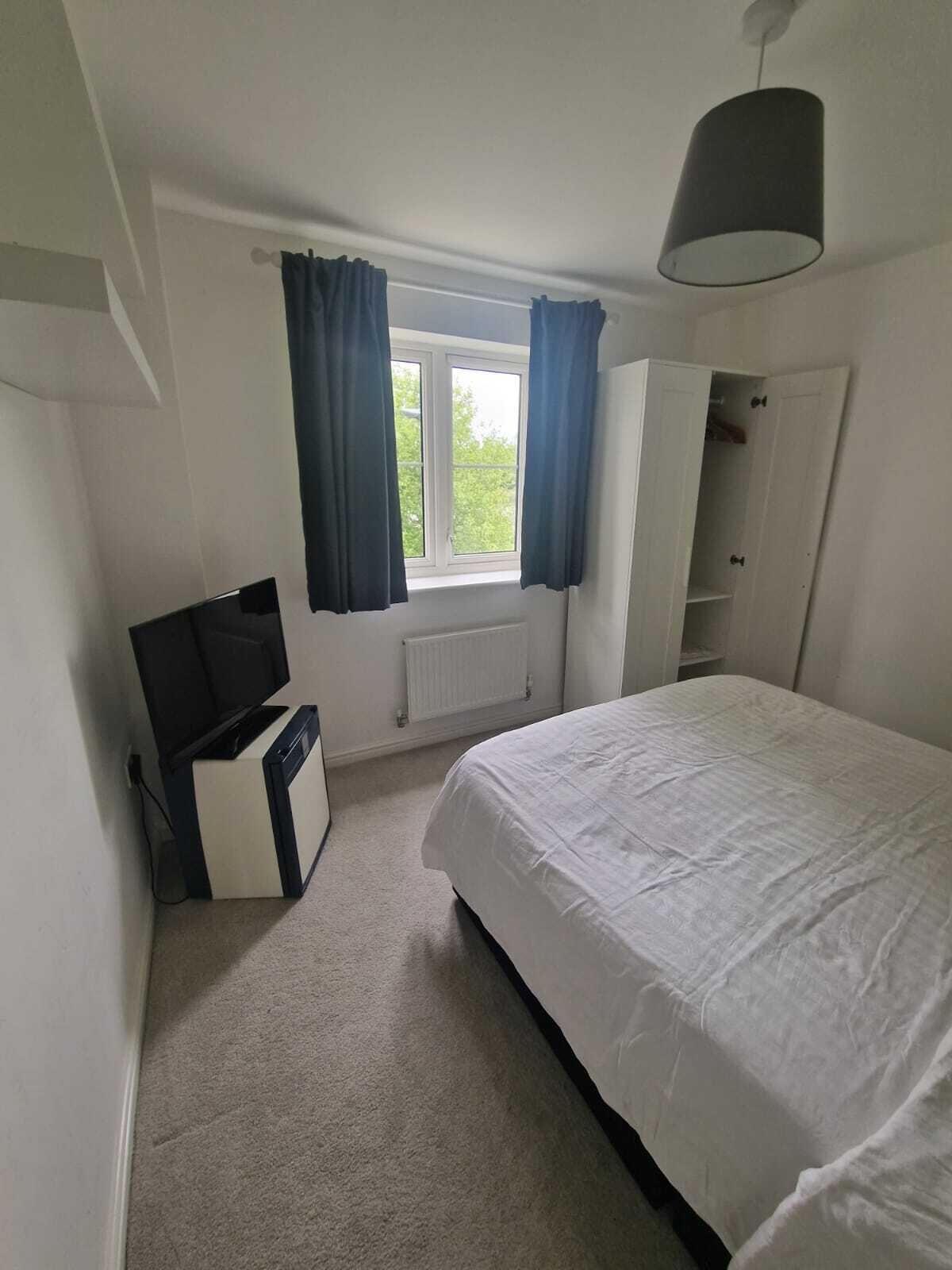 A bedroom with a bed, a wardrobe, a radiator, a window with curtains, and a television.