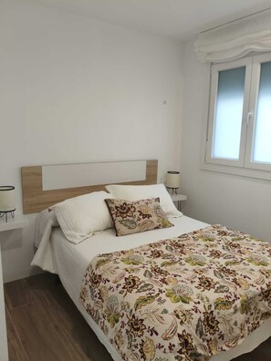Un dormitorio con cama, cabecera, mesitas de noche, ventana y lámpara de pie.