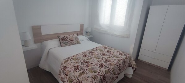 Una cama individual con colcha de estampado floral, cabecera de madera, lámparas de noche y un armario.