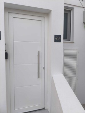 Eine weiße Tür mit Griff, darüber ein kleines Fenster und eine Adlerschild mit der Hausnummer.