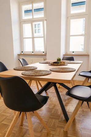 A dining area with a wooden table, black chairs, woven placemats, and a potted plant. - Gera Apartment Green foosball table 8 guests (Gera)