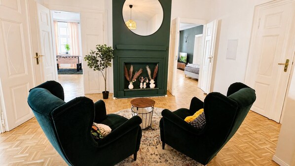 A living room with dark green armchairs, a round coffee table, and a fireplace with decorative items. - Gera Apartment Green foosball table 8 guests (Gera)