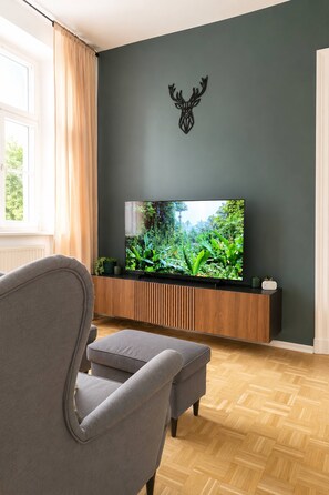 A modern living room with a flat-screen TV mounted on a wooden console, a grey armchair, and a decorative deer head on the wall. - Gera Apartment Green foosball table 8 guests (Gera)