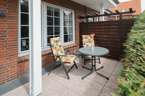An outdoor patio with a table and two chairs, a wooden fence, and a brick wall. - "East" in the Lauwersoog house (Juist)