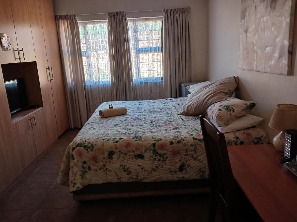 Un dormitorio con cama, televisión, mesa y cortinas.