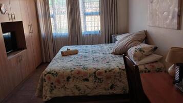Un dormitorio con cama, televisión, mesa y cortinas.
