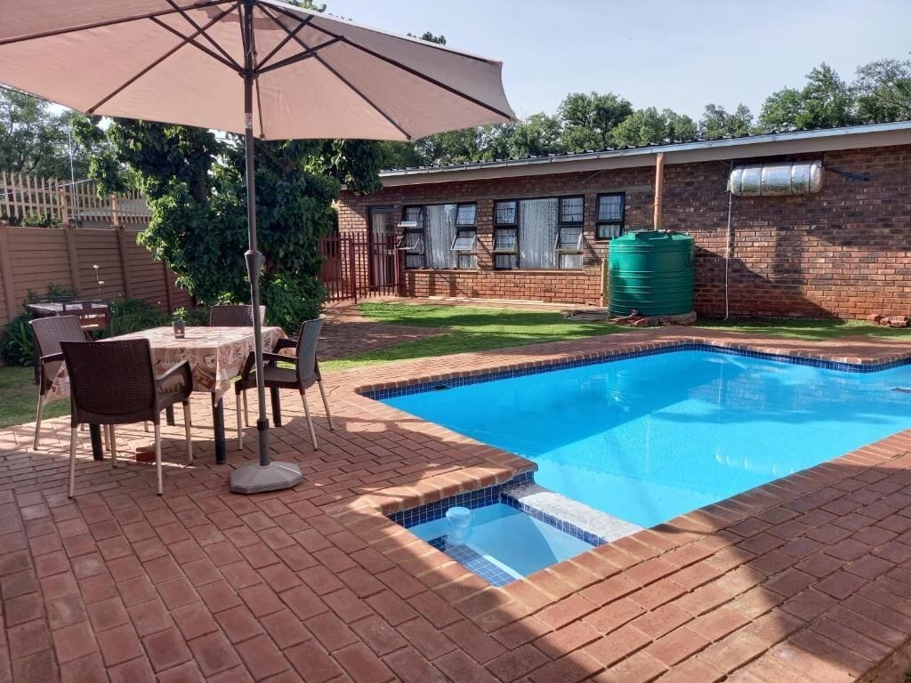 Une piscine avec une terrasse en briques, une table avec des chaises et un grand parasol.
