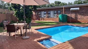 Une piscine avec une terrasse en briques, une table avec des chaises et un grand parasol.