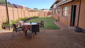 Un espace extérieur aménagé en patio, avec un sol en briques, une table ronde entourée de chaises et un coin salon abrité.