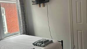Un dormitorio con cama, televisor de pantalla plana en la pared, ventana con cortinas y una puerta.