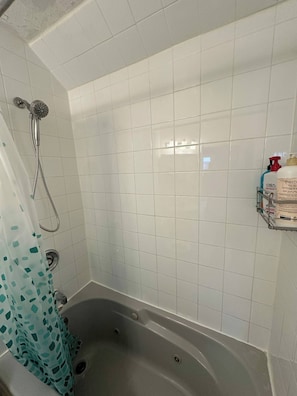 A bathroom with a bathtub, a showerhead, and a shelf with toiletries.