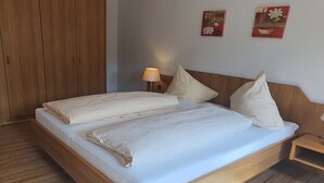 Een bed met houten frame, een nachtkastje met een lamp en twee aan de muur hangende schilderijen.