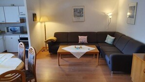 Een knus woongedeelte met een bank, een eettafel, een lamp en een magnetron in de keuken.