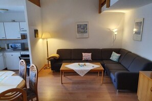 Ein kompakter Wohnraum mit Sofa, Esstisch, Lampe und Mikrowelle in der Küchenzeile.