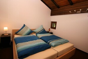 Una cama con ropa de cama azul, una mesita de noche con una lámpara y un pequeño marco de fotos en la pared.