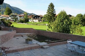 Un patio con mesa y sillas, pared de ladrillo y vistas a casas y árboles.