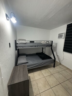 A bunk bed room with a desk, a wall-mounted light, and a window with blinds. - Your Adventure Home El Yunque, Culebra & Icacos (Luquillo city)