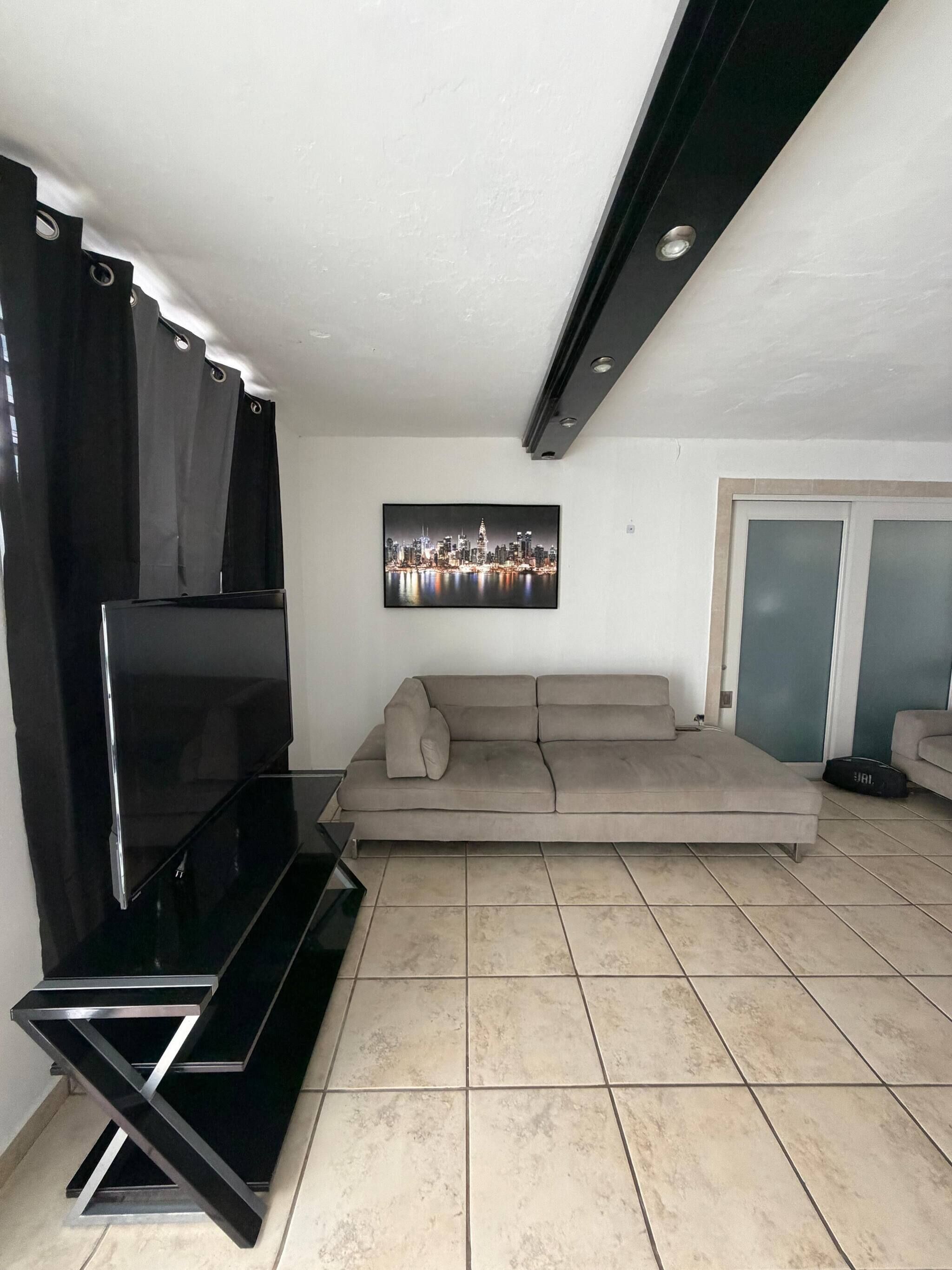 A living room with a flat-screen TV, a sofa, and a cityscape painting.