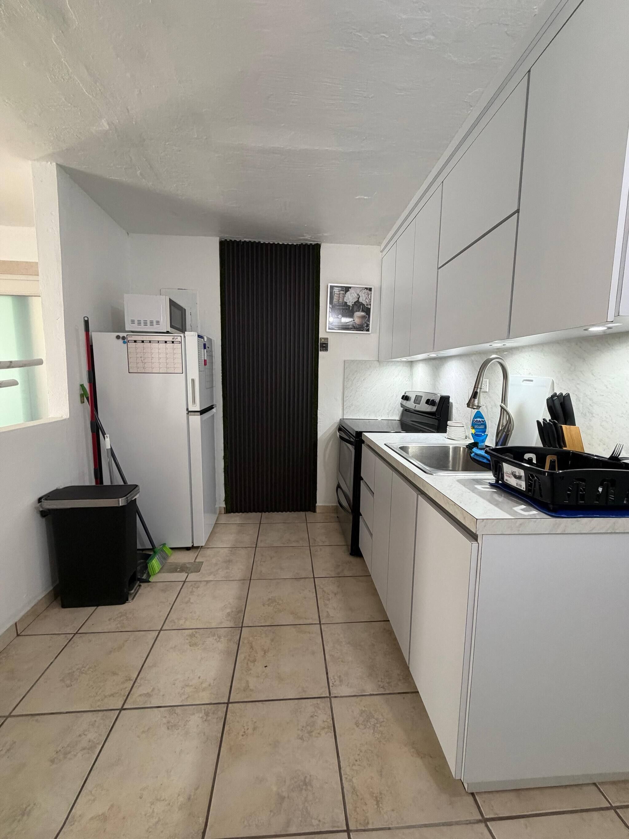 Una cocina compacta con refrigerador, microondas, estufa, fregadero y un pequeño bote de basura.