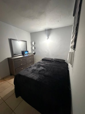 A bedroom with a bed, a dresser, a mirror, and a wall-mounted light fixture. - Your Adventure Home El Yunque, Culebra & Icacos (Luquillo city)