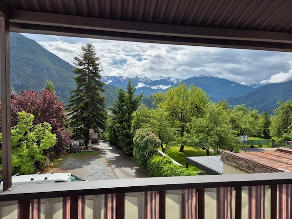 Ein Balkon mit Blick auf eine Berglandschaft, Bäume und einen gepflasterten Weg.