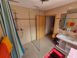 Ein Badezimmer mit Duschkabine aus Glas, Waschbecken, Spiegel und Handtuchhalter mit bunten Handtüchern.