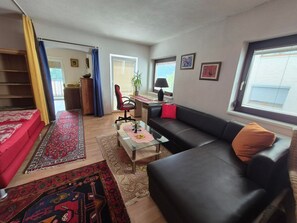 Ein Wohnzimmer mit einer Couch, einem Couchtisch, einem Schreibtisch mit Stuhl und einem Fenster mit Jalousien.