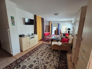 Ein kompakter Wohnbereich mit Küchenzeile, einer Sofagarnitur, einem Esstisch und einem an der Wand befestigten Fernseher.