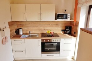A compact kitchen with white cabinets, a microwave, a coffee maker, and a bowl of fruit on the counter. - Holiday apartment with 2 bedrooms (Pottenstein)