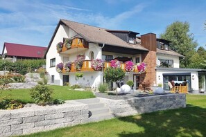 Ett modernt hus i två våningar med en balkong, stentrappor och en välskött trädgård.