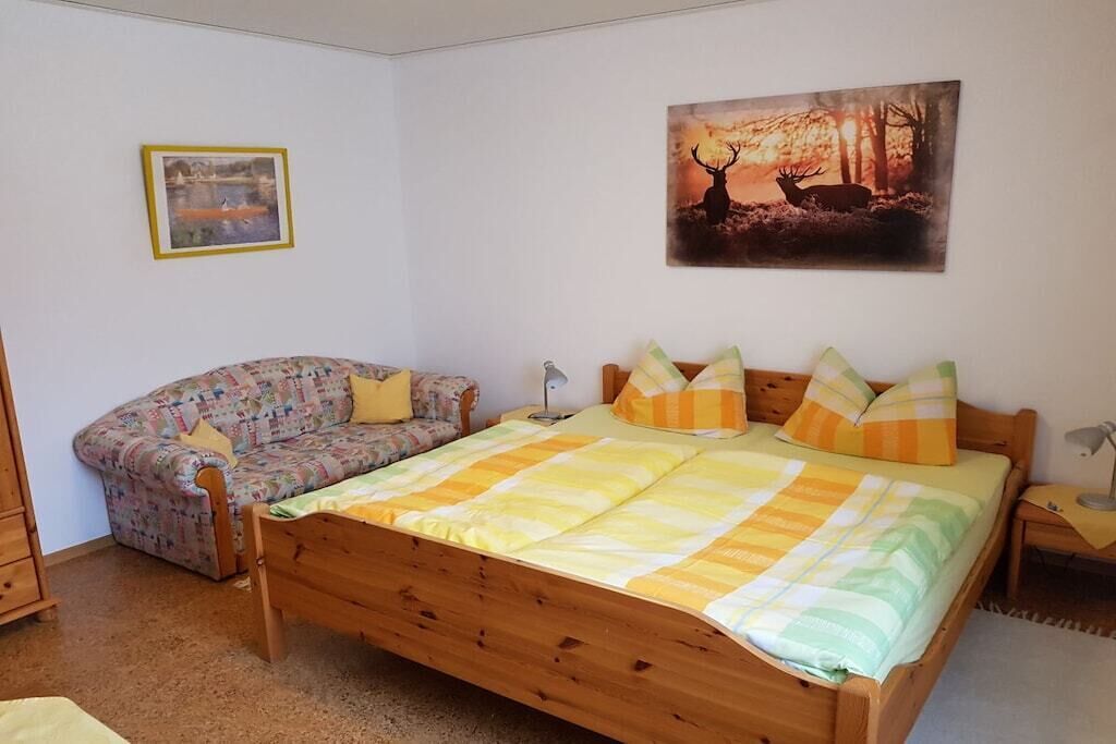 Un dormitori amb un llit de fusta, un sofà estampat, un quadre de cérvols i una fotografia emmarcada a la paret.