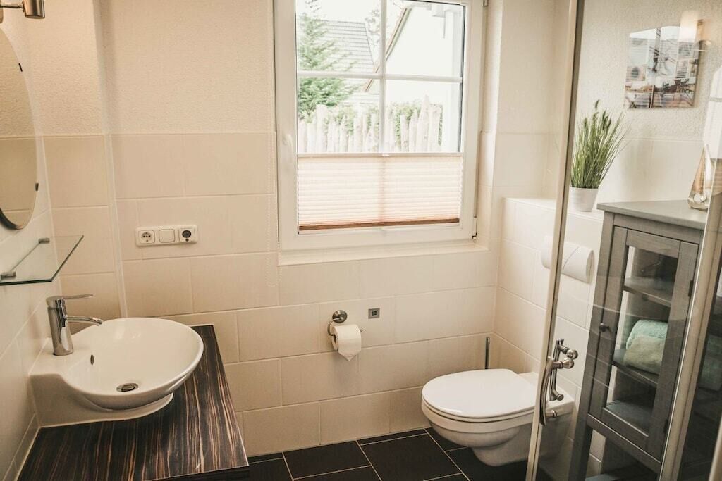 Ein Badezimmer mit weißem Waschbecken, Toilette und einem Fenster mit Jalousien.