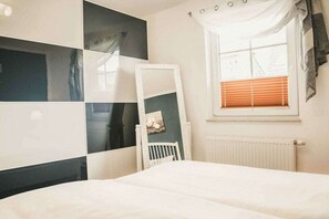 Ein Schlafzimmer mit einem Bett, einem weißen Stuhl, einem Fenster mit Jalousien und einer Heizung.