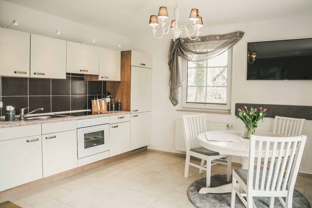 Une cuisine moderne avec des armoires blanches, un four encastré et un coin repas comprenant une table ronde et des chaises blanches.