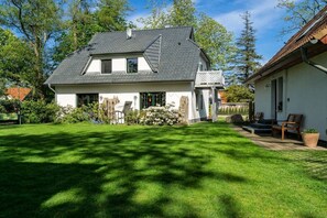 A two-story house with a sloped roof, a front porch with seating, and a well-maintained lawn. - Holiday apartment with 1 bedroom (Ostseebad Prerow)