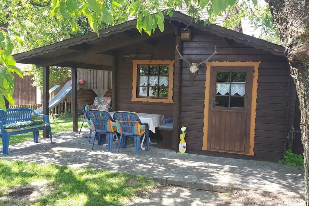 A wooden cabin with a porch, a table, and chairs.