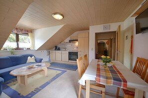 A cozy living room with a sofa, coffee table, and a dining area with a table set for two. - Holiday apartment with 1 bedroom (Pottenstein)