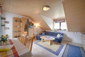 Ein gemütliches Wohnzimmer mit einem blauen Sofa, Holzmöbeln und einem Essbereich mit Tisch und Stühlen.