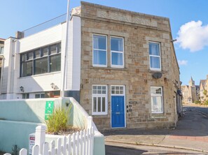 A two-story stone building with a blue door, white windows, and a sign indicating a fire assembly point. - Seafront Soleil (Penzance)