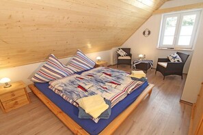 Une chambre avec un plafond en pente, un lit avec une literie à rayures, une chaise, un bureau et une fenêtre.