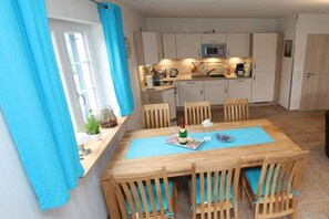 Un coin repas avec une table et des chaises en bois, une cuisine à l’arrière-plan et une fenêtre avec des rideaux.
