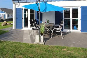 Une terrasse extérieure avec une table et des chaises, un parasol bleu et une plante en pot.