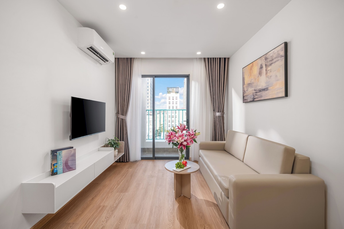 Una sala de estar moderna con un televisor de pantalla plana, un sofá, una mesita con un jarrón de flores y un cuadro en la pared.