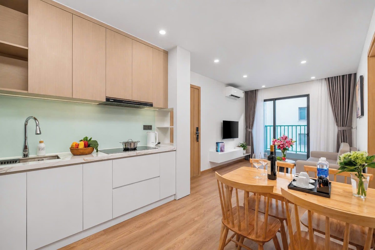 Una cocina moderna con armarios blancos, horno empotrado y comedor con mesa y sillas de madera.
