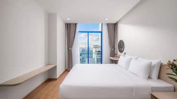 Habitación de hotel moderna con una cama grande, una mesita de noche, un escritorio pequeño y vistas de la ciudad a través de un ventanal amplio.