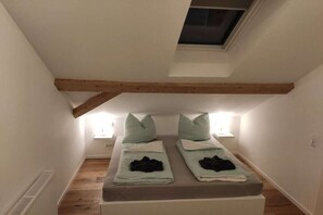 A small, cozy room with a sloped ceiling and a skylight. There are two beds with pillows and blankets, and a small table with a lamp. - Holiday apartment in Görisried with Wi-Fi (Görisried)