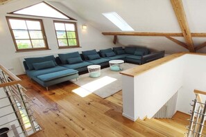 A loft-style room with a large sectional sofa, a small round table, and a staircase. - Holiday apartment in Görisried with Wi-Fi (Görisried)