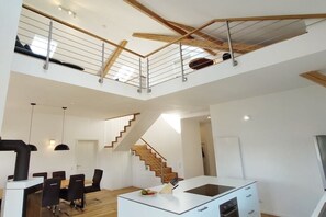A modern kitchen with a central island, wooden staircase, and a dining area with chairs and a table. - Holiday apartment in Görisried with Wi-Fi (Görisried)