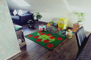 A cozy living room with a sofa, a coffee table, and a rug with ladybug designs. - Dreaming by the fireplace (Wangerland)